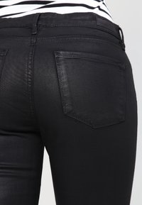 Svarta denimjeans med slim fit, med en distinkt design på bakfickan och en slät, något glänsande yta.