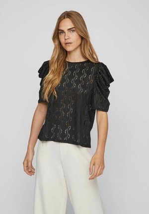 Black short-sleeve top with textured pattern and puffed sleeves. Lightweight fabric features wavy cutouts, paired with white wide-leg trousers.