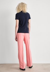 Marineblå polo-skjorte og lys rosa vide bukser. Skjorten har en glatt tekstur, mens buksene er laget av et teksturert, lett stoff.