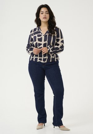 Blouse à manches longues et décolleté en V en crème avec un motif abstrait bleu marine, associée à un jean foncé ajusté et des escarpins beiges à bout pointu.
