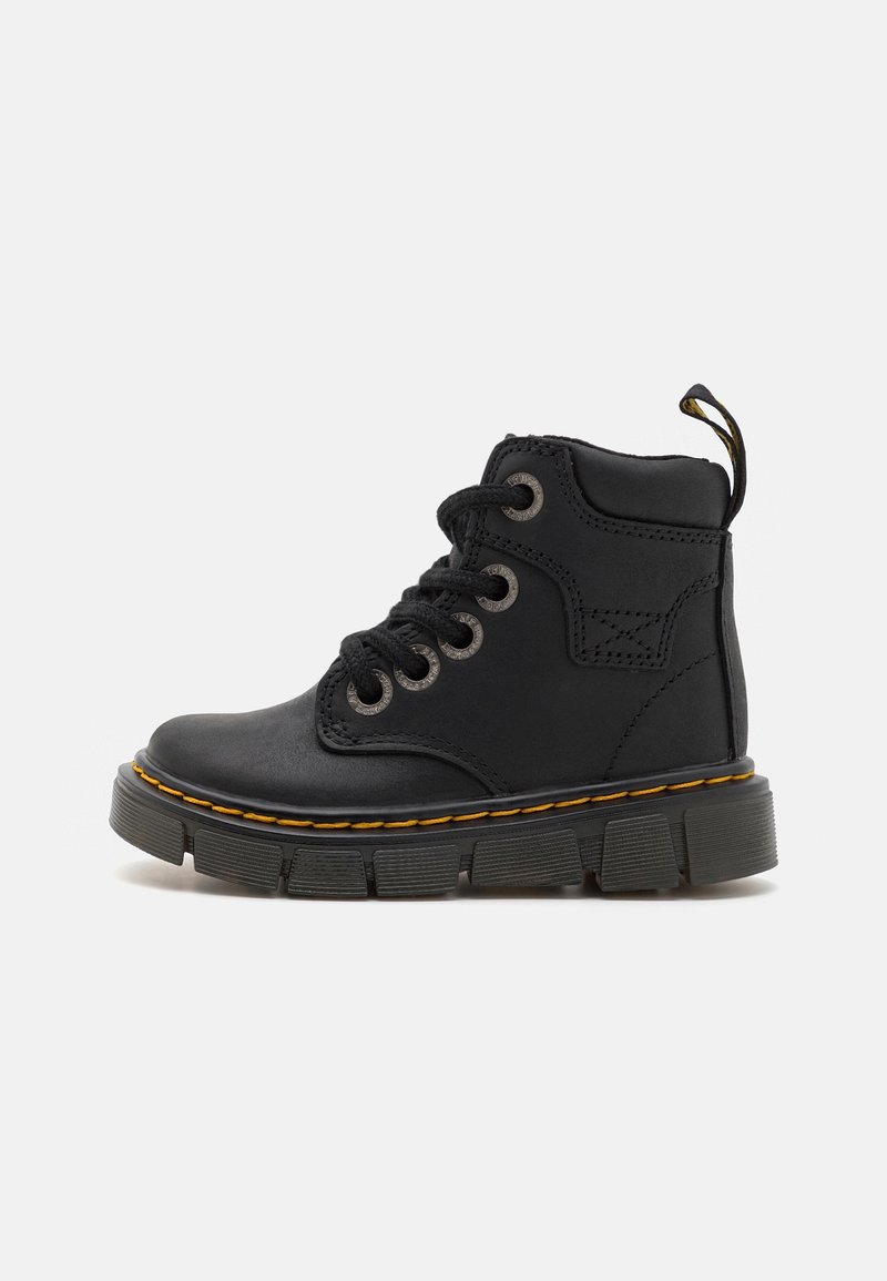 Boots en cuir noir avec semelle épaisse rainurée, coutures jaunes, col rembourré, laçage à l'avant et languette sur fond blanc.