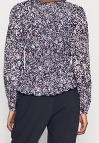 Blusa peplum floreale di colore blu scuro con vivaci motivi rosa, bianchi e blu. Presenta arricciature e maniche elastiche.