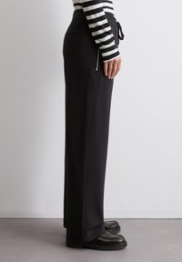 Zwarte high-waisted broeken met een trekkoord in de taille, voorzien van zijzakken en een rechtlijnige snit, gemaakt van een zachte, textuurrijke stof.