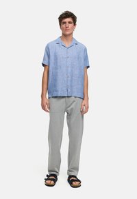 Lys blå kortermet knapp-up skjorte laget av lin, sammen med grå joggebukser og svarte sandaletter. Enkel, avslappet passform.