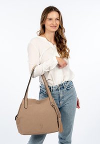 Beige textured handbag with a crescent shape, dual shoulder straps, and a side tassel detail. Made of durable synthetic material.