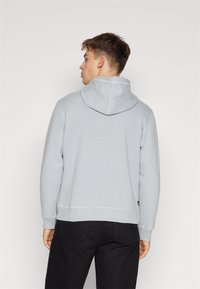Felpa leggera grigia con cappuccio, con coulisse e tasca a marsupio, caratterizzata da una morbida texture e polsini a coste, abbinata a pantaloni neri.