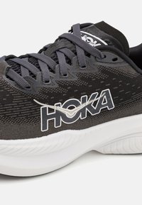 Schwarzer Sport-Schuh mit Mesh-Obermaterial, Schnürverschluss und auffälligem weißen HOKA-Logo. Dicke weiße Zwischensohle für Polsterung und strukturiertes Gummi-Außensohle.