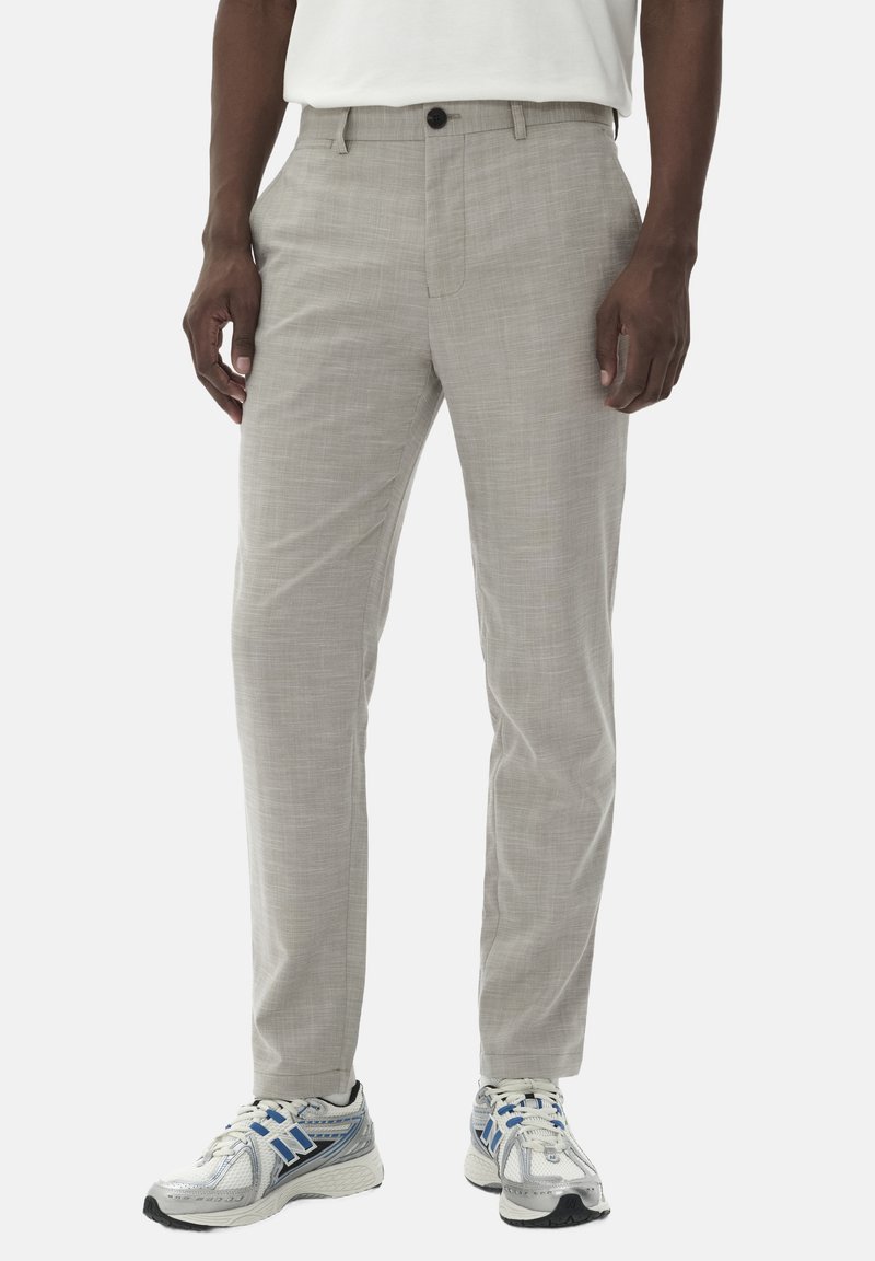 Hellgraue Hose aus strukturiertem Stoff, mit einem einzigen Knopfverschluss und geradem Bein, kombiniert mit weißen Sportschuhen.