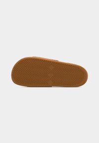 Suela de goma de una sandalia tipo slide marrón con un patrón de espiga y una marca en forma de diamante en el centro.