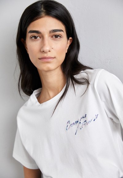 Weißes Baumwoll-T-Shirt mit lockerer Passform. Verfügt über ein blaues und lila gesticktes Textdesign auf der Brust sowie einen einfachen Rundhalsausschnitt.