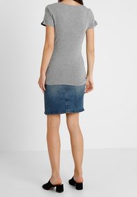 Camiseta de manga corta gris combinada con una falda mini de mezclilla oscura. La falda tiene un dobladillo deshilachado, y el conjunto se completa con unos zapatos negros de tipo slip-on.
