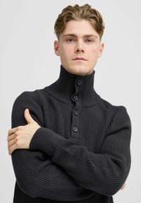 Pulover negru cu nervuri, cu guler înalt și placket cu cinci nasturi, având un material texturat și mâneci lungi.
