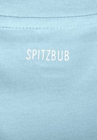 Helles blaues Gewebe mit einem strukturierten Strickmuster, mit dem Wort "SPITZBUB" in Weiß auf der Rückseite in der Mitte gestickt.
