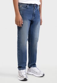 Μπλε τζιν παντελόνι με ίσια εφαρμογή, ανοιχτό πλύσιμο και διακριτικό ξεθώριασμα. Διαθέτει πέντε τσέπες και πορτοκαλί λογότυπο στη ζώνη μέσης.