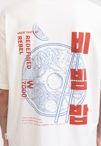 Maglietta color crema con testo grafico blu e rosso e un'illustrazione dettagliata di una ciotola di cibo con bacchette.