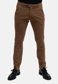 Chino marroni con vestibilità slim, dotati di chiusura a bottoni e tasche laterali, abbinati a scarpe nere a punta. Tessuto liscio e linee pulite.