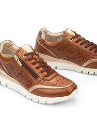 Zapatillas de cuero marrón con detalles perforados, acentos dorados, cordones en la parte delantera y cremallera lateral. Cuenta con una suela blanca y un interior acolchado.