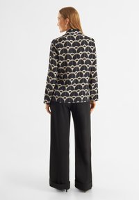 Blazer a motivi neri e oro con design ad arco, dotato di colletto e maniche lunghe, abbinato a pantaloni neri a gamba larga.