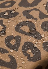 Vandafvisende stof med en tan baggrund, der har sorte leopardpletter, og viser dråber af vand på overfladen.