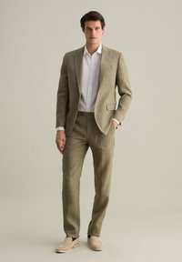 Hellbeige Leinenanzug mit schmaler Passform, bestehend aus einem Ein-Knopf-Jacket, Reverskragen und passenden Hosen. Getragen mit einem weißen Hemd mit Kragen.