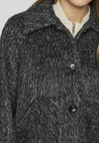 Pelēka vilnas jakas ar teksturētu apdari, liels apkakles, un divas priekšējās kabatas. Ar melnām pogām un ribotām krēmbaltiem iekšējo apkakli.