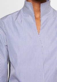 Randig skjorta i blått och vitt med hög krage, med en framplacket och texturerat tyg. Vertikala ränder skapar en klassisk look.