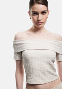 Top de color crema, sin mangas y con textura, de silueta ajustada. Diseño sencillo con un patrón ondulado y suave.