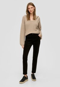 Pull en tricot beige avec un col en V et une capuche, pantalons en velours noir, et baskets noires avec une épaisse semelle claire.