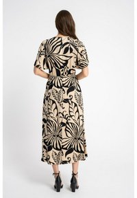 Długa, zwiewna sukienka z krótkimi rękawami, z czarnym kwiatowym wzorem na beżowym tle. Elastyczny pas z luźnym krojem. Czarne szpilki.
