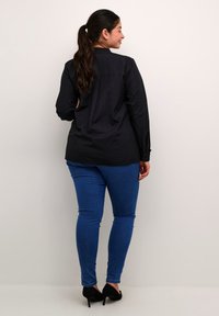Sort skjorte med knapper og en rygfold, parret med blå tætsiddende jeans og sorte stiletter. Glat stof, klassisk design og tætsiddende silhuet.