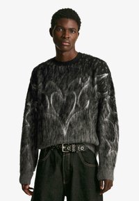 Szürke kötött pulóver, texturált, bolyhos anyagból, fehér absztrakt szívmintával. Kerek nyakkivágású és bordázott mandzsettával. Fekete, studdal díszített öv.