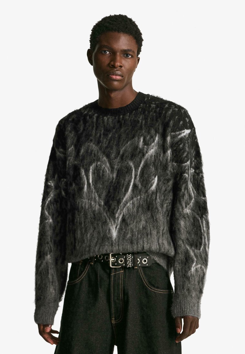 Szürke kötött pulóver, texturált, bolyhos anyagból, fehér absztrakt szívmintával. Kerek nyakkivágású és bordázott mandzsettával. Fekete, studdal díszített öv.