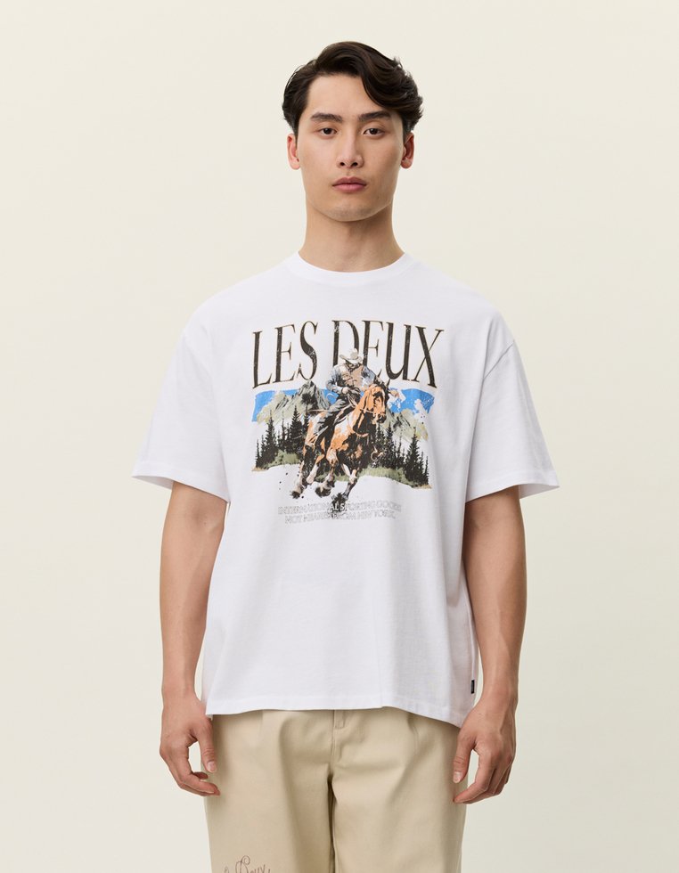 Biała bawełniana koszulka z grafiką przedstawiającą jeźdźca konnego, góry i drzewa; luźny krój, krótkie rękawy i okrągły dekolt.