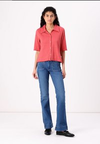 Rode kortmouwen overhemd met knopen en een ribbeltextuur, gecombineerd met blauwe flared jeans en zwarte schoenen. Eenvoudige kraag en cropped ontwerp.