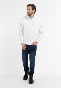 Felpa bianca con tasca frontale e cordini, abbinata a jeans blu scuro e scarpe nere. Design semplice, tessuto morbido.