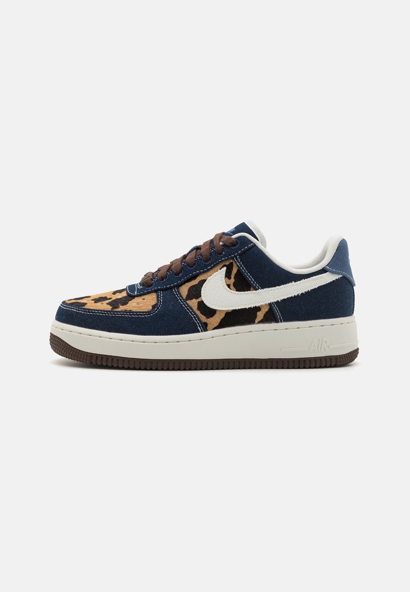 Baskets basses en denim bleu foncé, panneaux imprimé léopard, swoosh blanc, lacets marron, semelle intermédiaire blanche avec semelle extérieure marron.