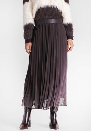 Vrouw draagt een geplooide donkere rok, zwarte enkellaarsjes met hak en een lange mouw pluizige trui met zwart-witte kleurvlakken.