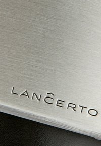 Metalowa płytka o szczotkowanej stalowej powierzchni, z wygrawerowanym napisem "LANÇERTO." Napis umieszczony w dolnym rogu, czysty design.