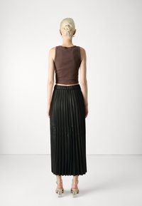 Brown cropped tank top paired with a black pleated midi skirt. The skirt has a smooth texture and an elastic waistband. Clear block-heeled shoes.