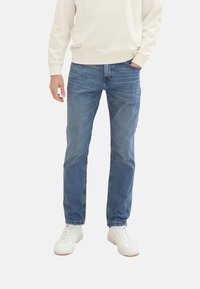 Vaaleansiniset farkut slim fit -mallilla. Ominaisuuksina viisi taskua ja vetoketjusuljenta. Yhdistettynä valkoisiin tennareihin ja vaaleaan villapaitaan.