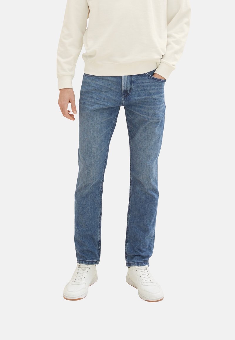 Vaaleansiniset farkut slim fit -mallilla. Ominaisuuksina viisi taskua ja vetoketjusuljenta. Yhdistettynä valkoisiin tennareihin ja vaaleaan villapaitaan.