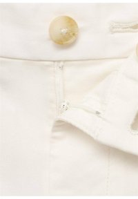 Gros plan sur un tissu en coton blanc avec un grand bouton de couleur marron clair, une fermeture éclair et des détails de couture. Le tissu est lisse avec un subtil éclat.