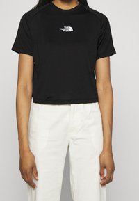 Svart kort t-shirt i lättviktstyg med korta ärmar och en vit logga på bröstet. Matchas med ljusa byxor.