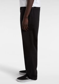 Black trousers with a straight leg design, made from smooth fabric. Features an elastic waistband and side pockets, paired with black sneakers.