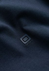 Tissu texturé foncé avec un logo carré simple et le texte "ombre" imprimé en dessous, montré en gros plan.