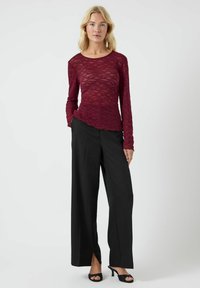 Top in pizzo bordeaux a maniche lunghe con finitura testurizzata, abbinato a pantaloni neri a gamba larga con vita alta e tacchi neri open-toe.