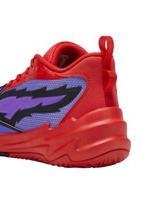 Zapatilla deportiva con un diseño en rojo y púrpura, parte superior de malla texturizada, acentos en negro y una suela de goma roja gruesa y ondulada.