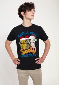 Sort t-shirt med tre stuffed characters iført røde juleskæg. Teksten siger "HAV EN MEGET Sooty JUL" i farverige bogstaver.