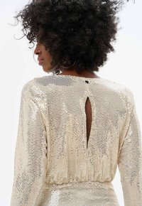 Robe dorée en sequins avec un col haut, des manches longues et un dos clé. Texture lisse avec une taille cintrée et une surface étincelante.