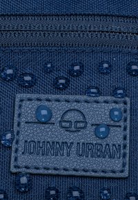 Blaues strukturiertes Gewebe mit Wassertropfen, versehen mit einem grauen, gestickten Etikett, das "JOHNNY URBAN" geprägt hat, und einem schlichten grafischen Design.
